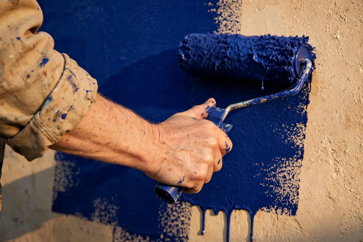 A painter rolling fresh ultramarine paint onto a warm plaster wall